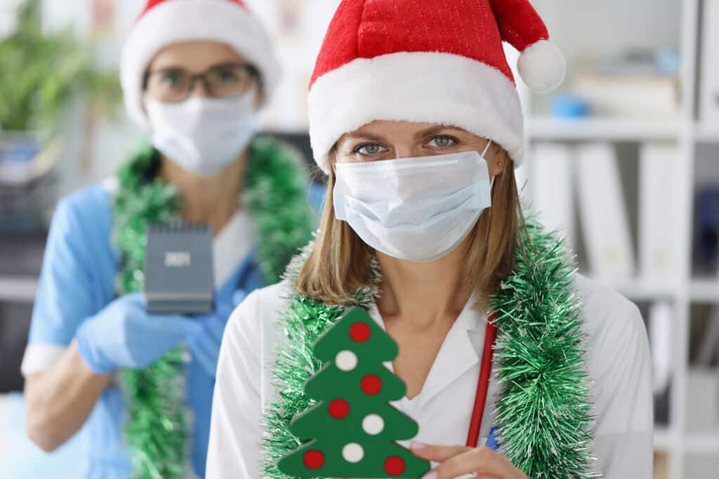 Two female doctors in protective medical masks and santa claus hats are smiling. Celebrating New Year and Christmas in hospitals near coronavirus pandemic concept