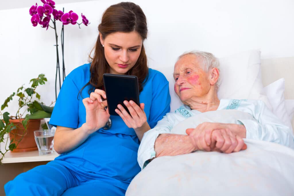 Caring nurse showing a digital tablet to an elderly woman in a nursing home.