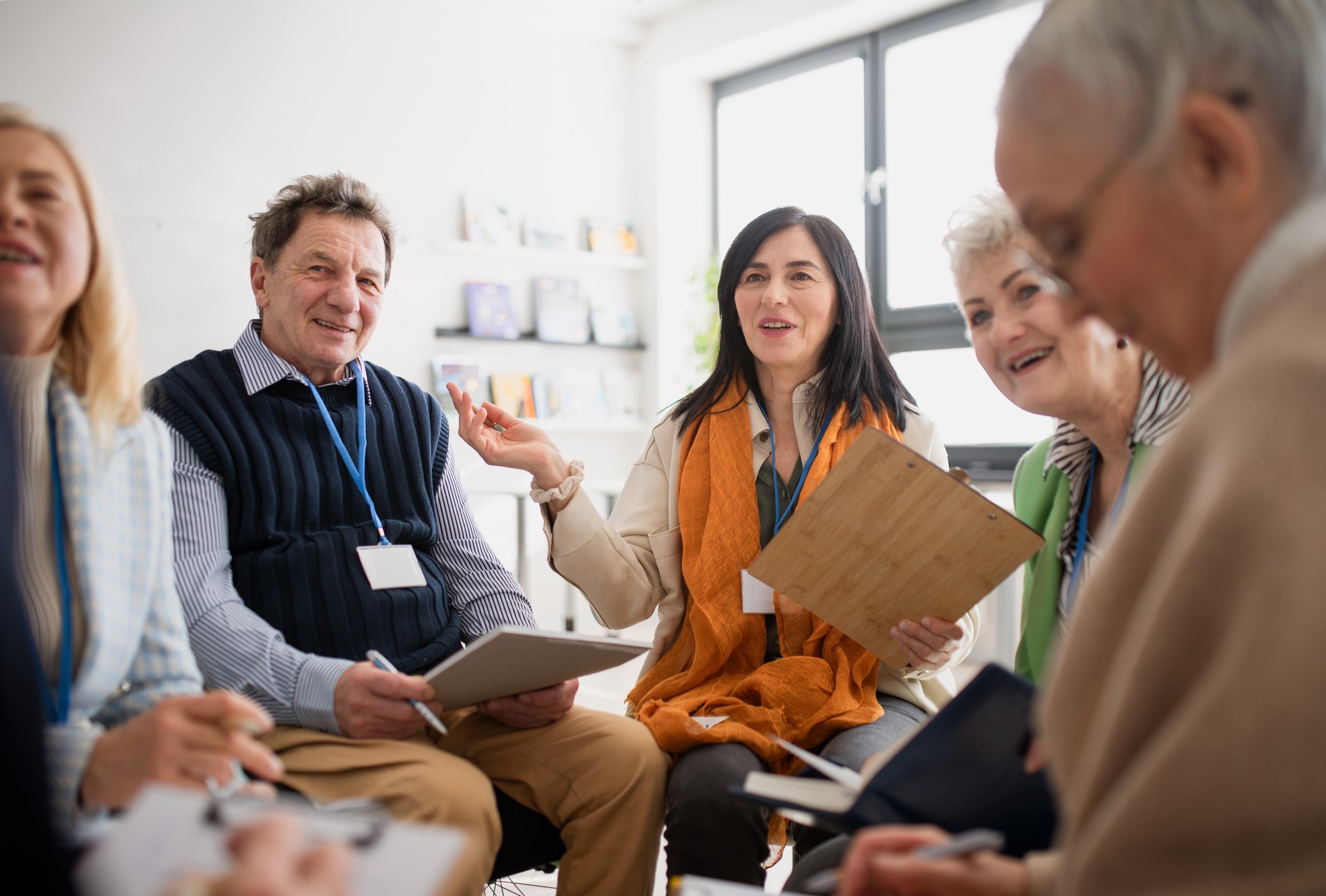 Excited elderly people attending a group therapy session at nursing house, positive senior man and woman sitting in circle, having conversation with psychologist