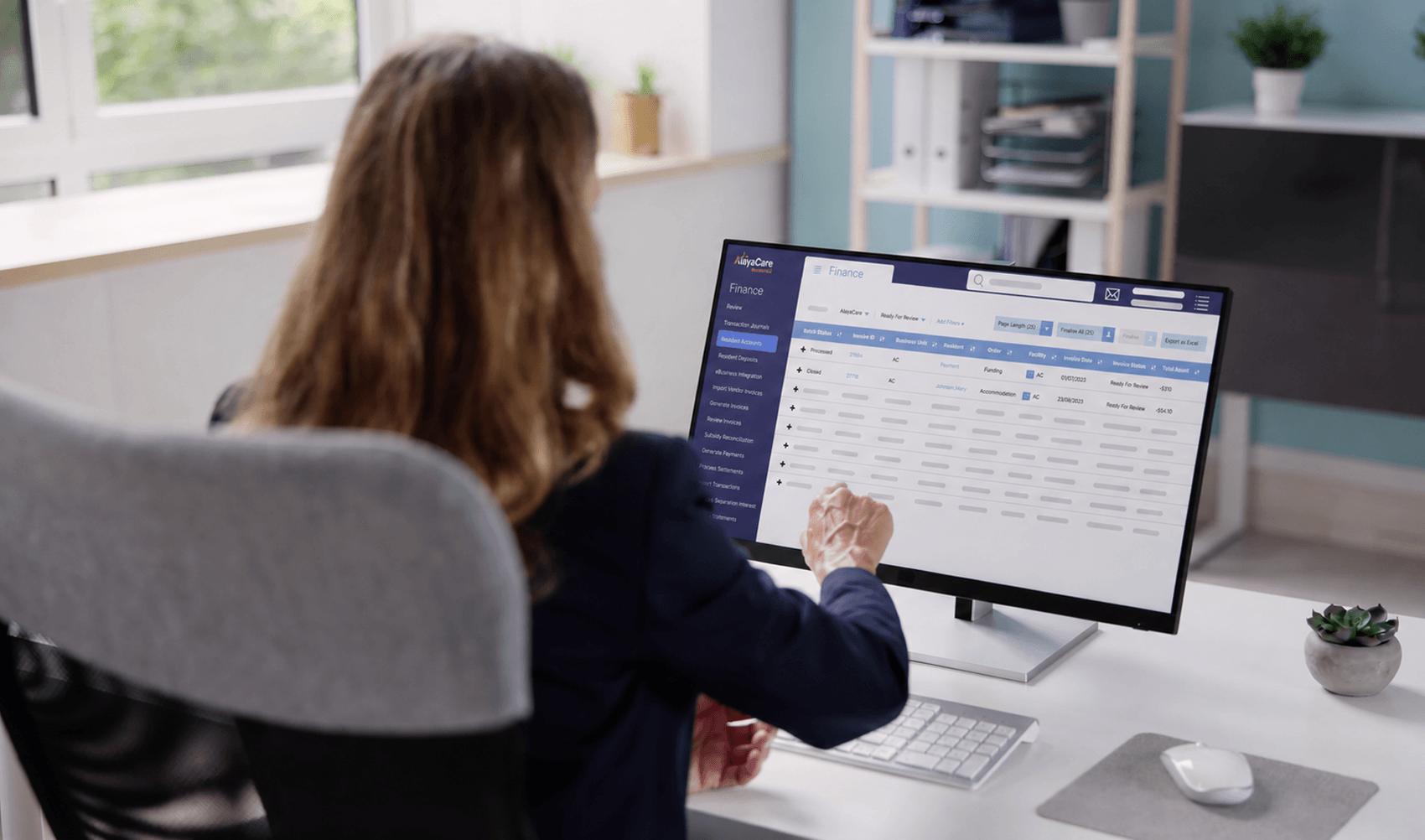 Office worker viewing an AlayaCare Finance resident accounts screen on a desktop monitor
