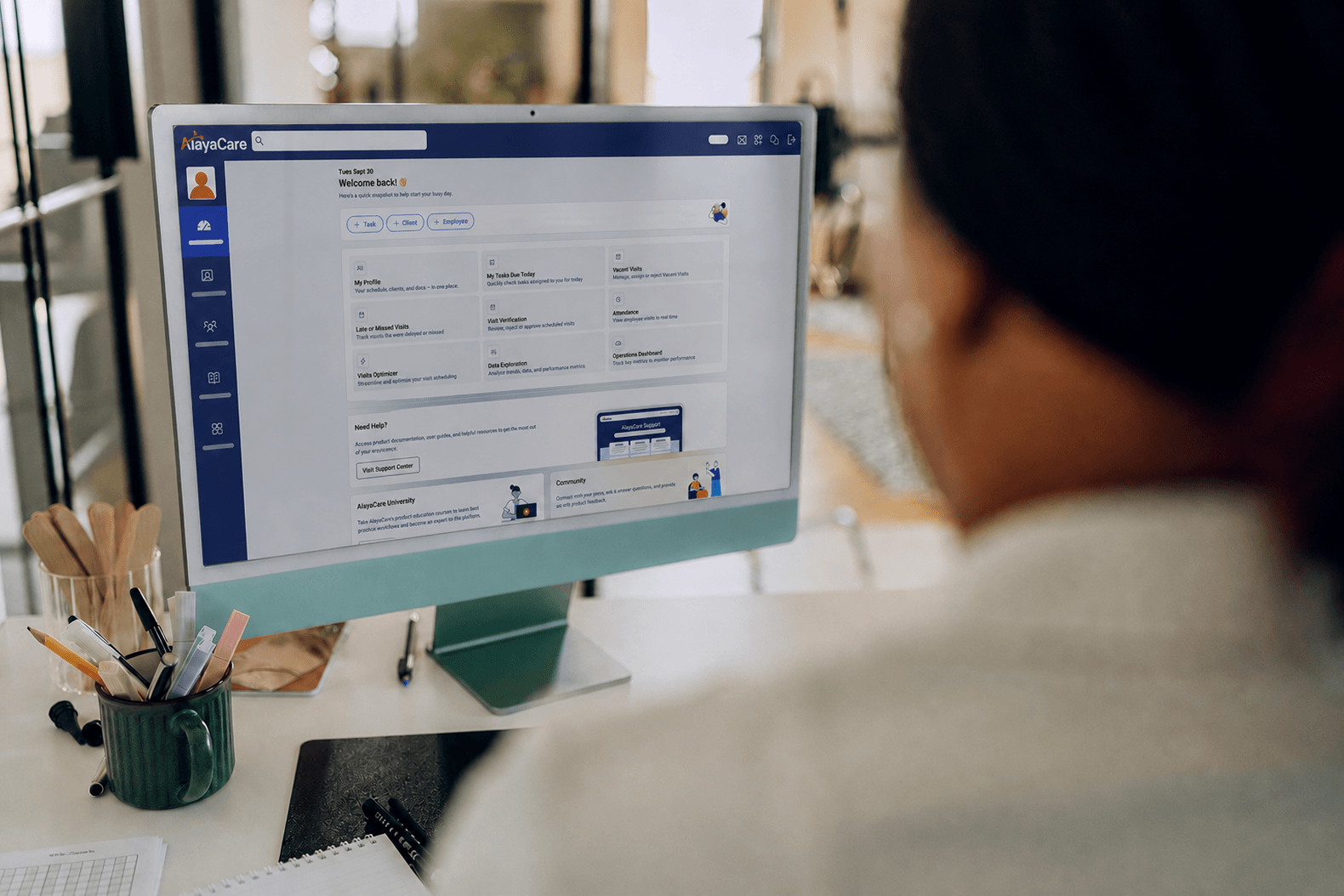 Office worker viewing an AlayaCare dashboard homepage on a desktop monitor