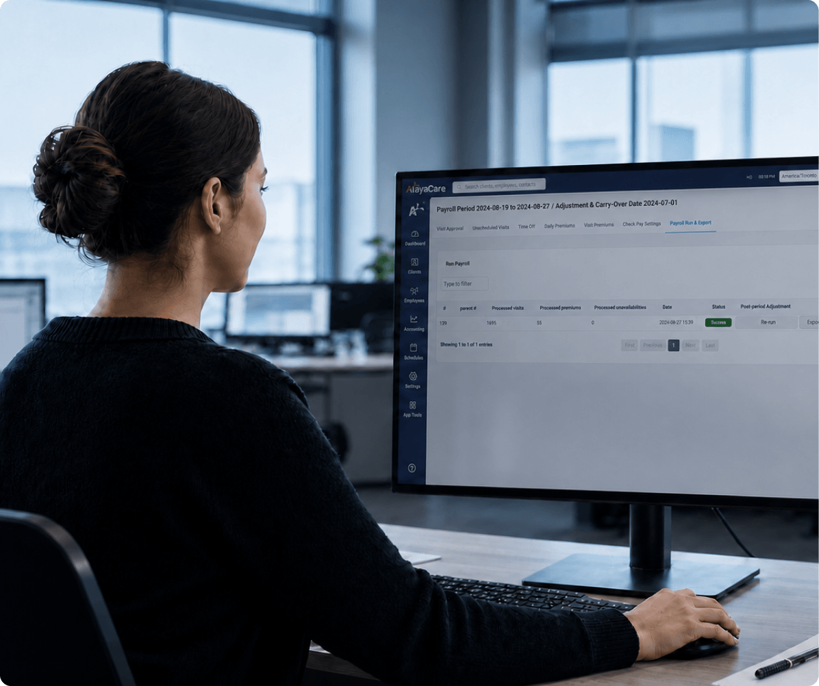 Office worker viewing an AlayaCare payroll run and export screen with a payroll period and adjustment date on a desktop monitor