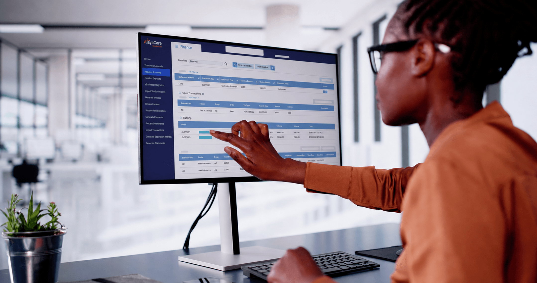 Office worker viewing an AlayaCare Finance resident accounts screen showing a tax invoice statement and capping transactions