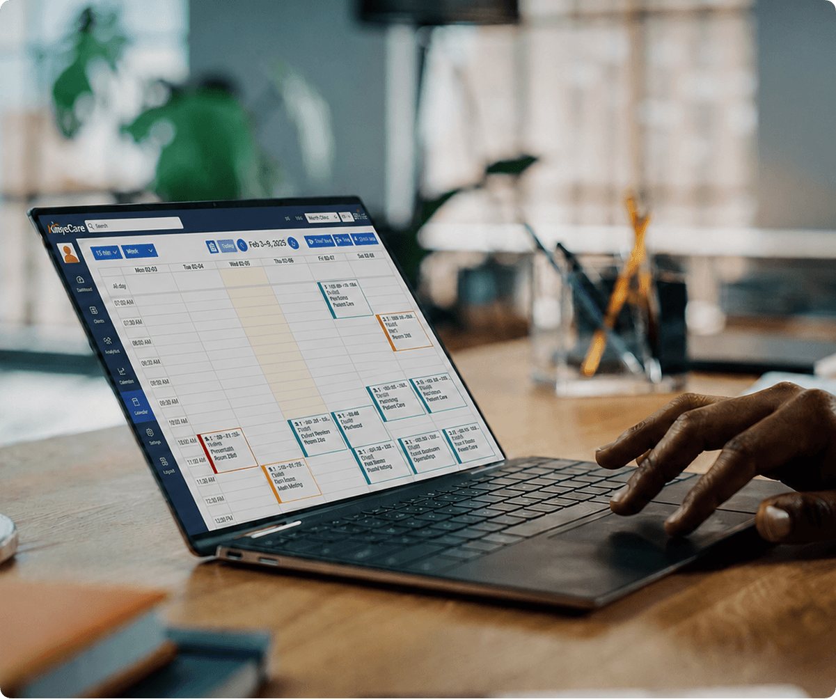 Office worker typing on a laptop displaying an AlayaCare weekly scheduling calendar with color-coded visits